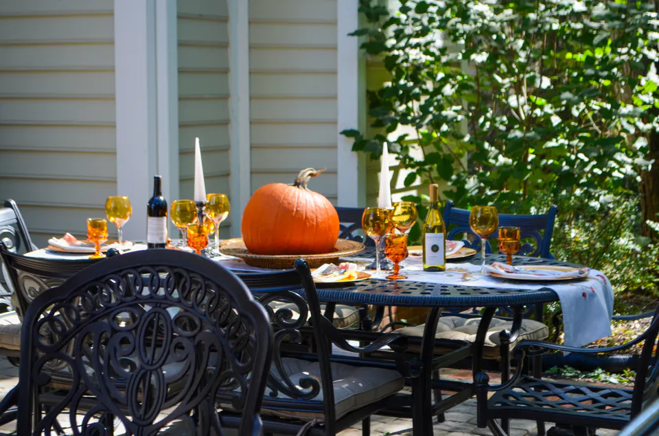 Close fall dining table with pumpkins, candles, chairs, paver patio, and shaded house-side garden.